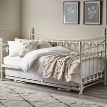 White day bed frame with spindle headboard, topped with pillows and a textured throw blanket