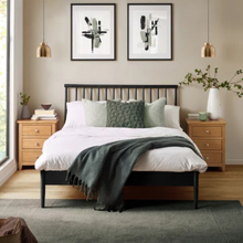 Bedstead with slatted headboard and dark frame, shown with pillows and blanket