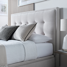 Upholstered ottoman storage bed side view with tall tufted headboard and gray upholstery