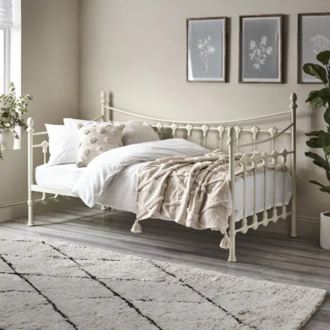 White day bed with spindle headboard and footboard, styled with pillows and layered bedding