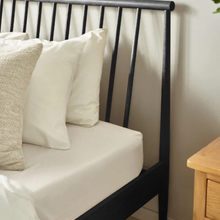 Bedstead side view with dark slatted headboard and white cushions