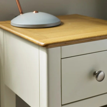 Oak-topped white bedside table with one drawer and round metal pull.