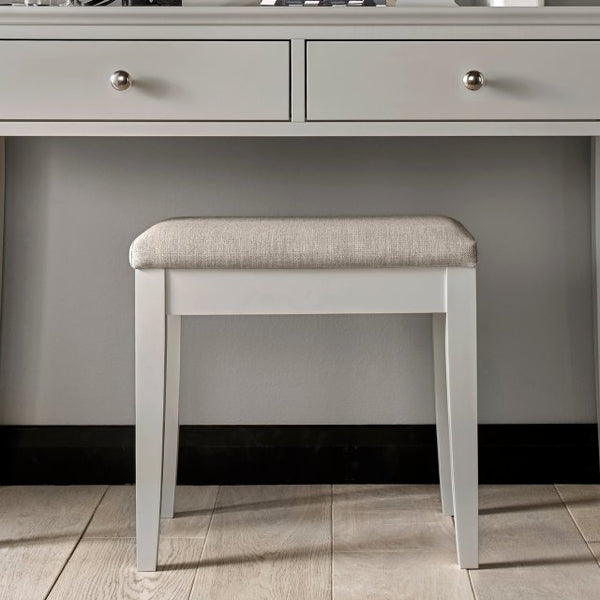 Soft grey upholstered stool with white frame and rounded padded seat
