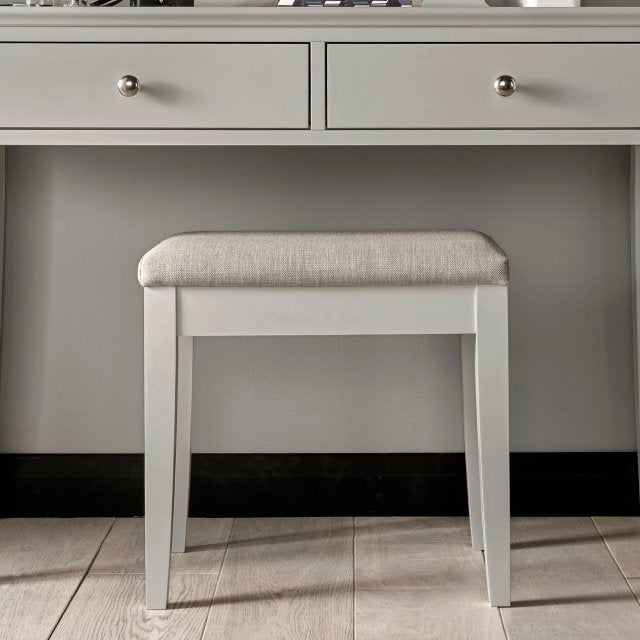 Soft grey upholstered stool with white frame and rounded padded seat