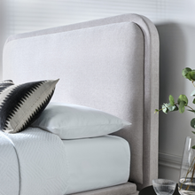 Light clay upholstered ottoman bed side view with rounded headboard and pillows