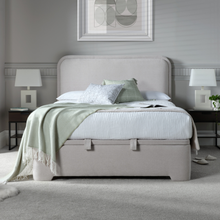 Light clay upholstered ottoman bed with pillows, quilted mattress, and side straps