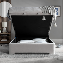 Upholstered ottoman bed with open storage compartment and light gray base, folded blanket